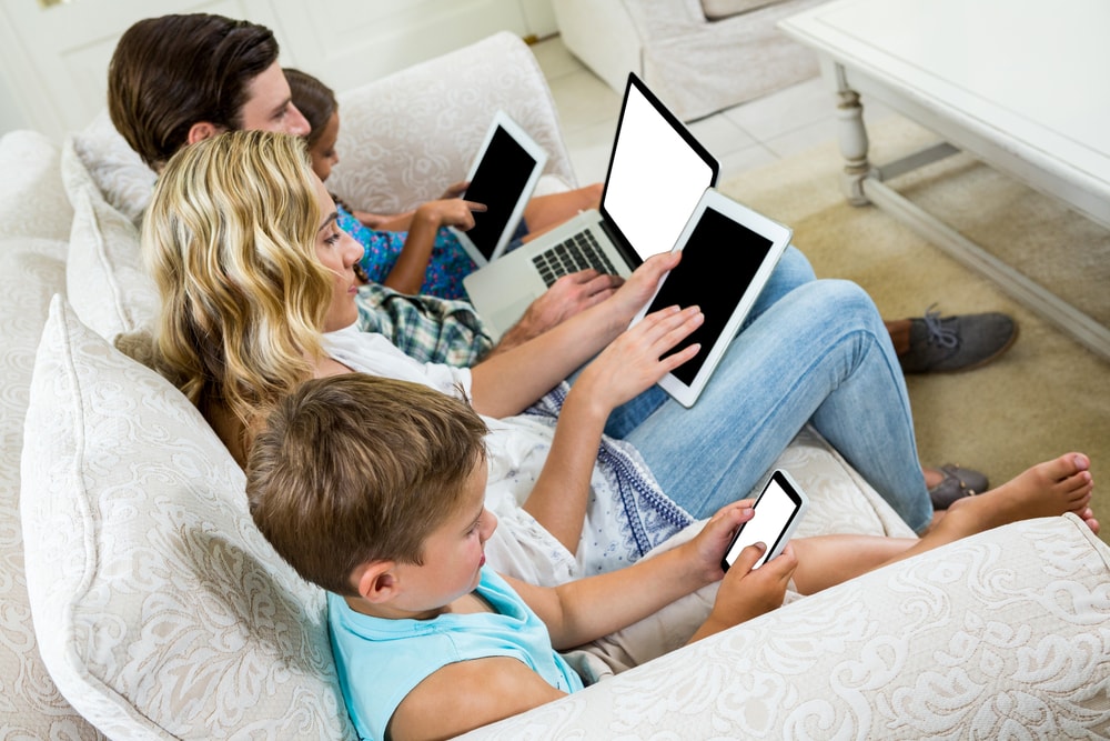Family spending screentime together on the couch with laptops, phones, and tablets.