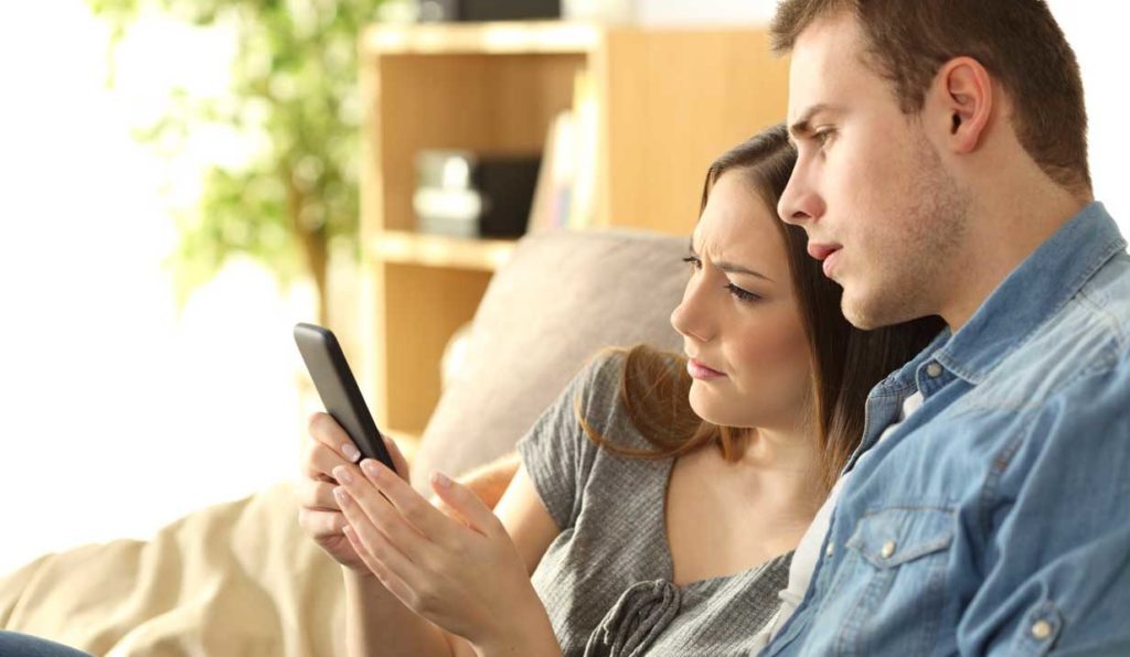 Women and Man reading with concern one cell phone in the man's hands with both on the sofa