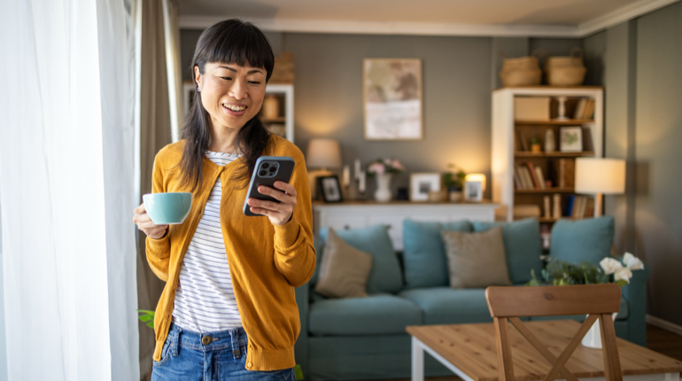 Woman happily using an iPhone 16 Pro Max at home, comparing features with Samsung Galaxy S25 Ultra.