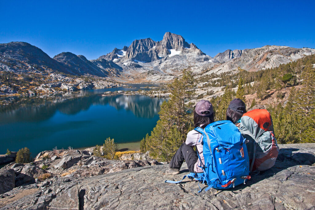 Two girls with backpacks sitting on top of hill, looking at a lake Thousand islands lakes, Eastern Sierra, California