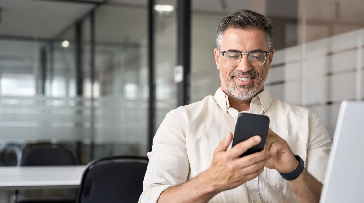 Man with glasses sitting in conference room smiling at his phone