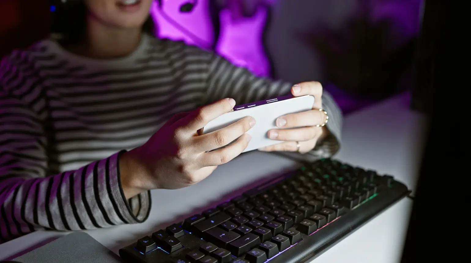 Close-up of person holding a smartphone horizontally in front of their computer