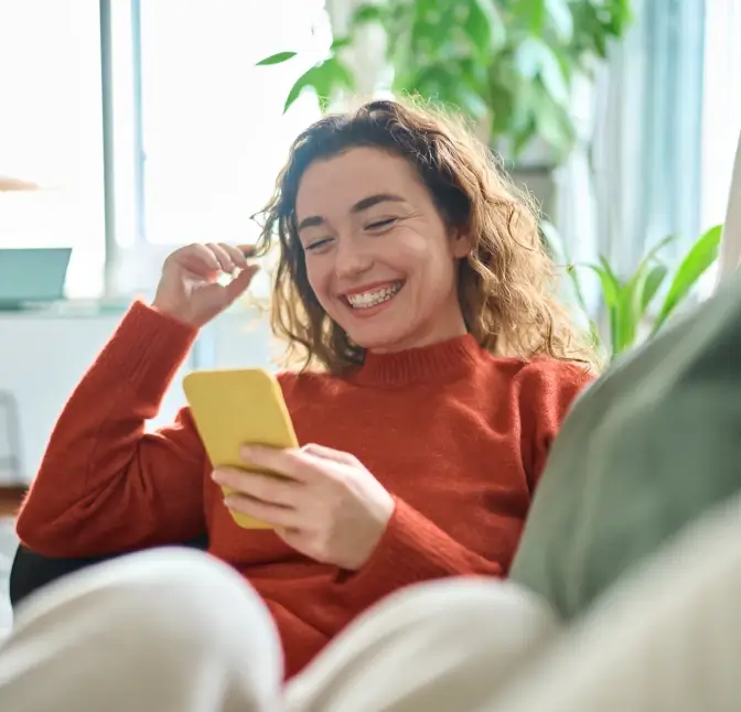 Woman with red sweater smiling while looking at her smartphone