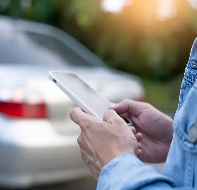 Person holding a tablet while standing next to a parked car outdoors.