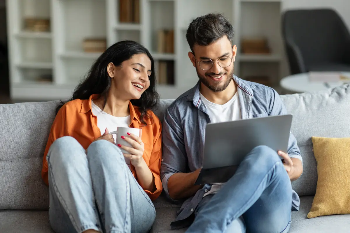 Smiling couple sitting on a couch looking at a laptop together in a modern living room.