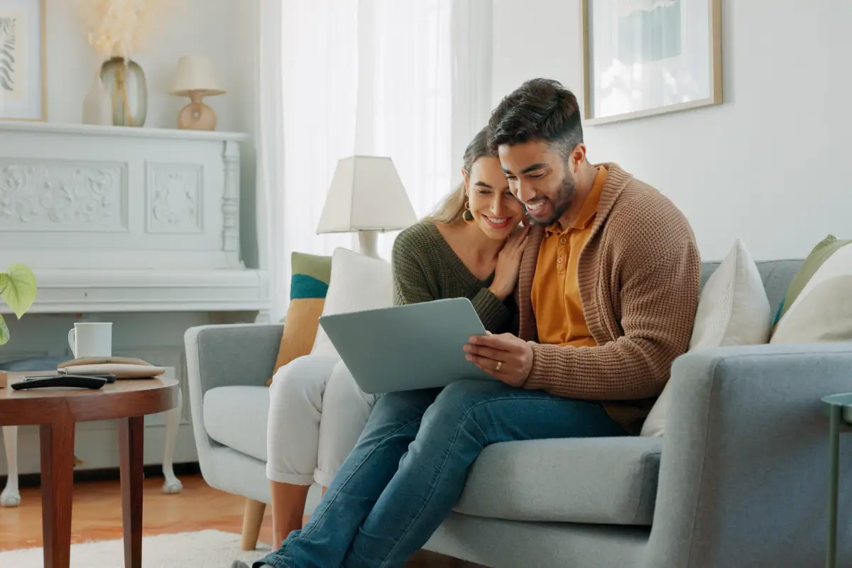Couple sitting on a couch looking at a laptop together in a cozy living room.