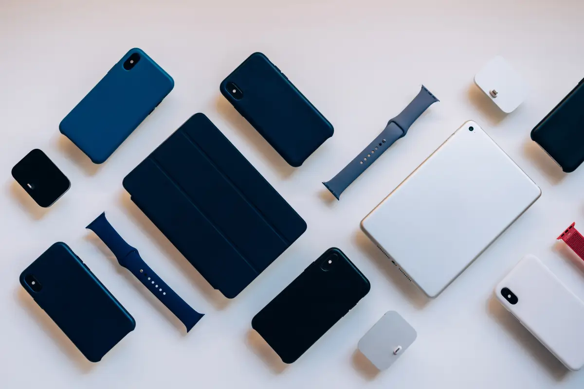 Flat lay of assorted Apple devices and accessories including iPhones, iPads, Apple Watch bands, and chargers on a white surface.