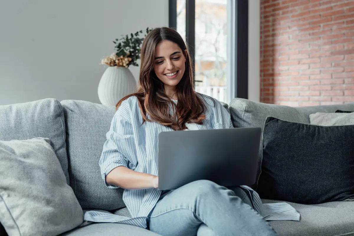 Woman sitting on a couch using a laptop in a cozy living room.