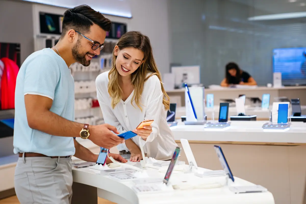 Customers comparing smartphones with a sales associate at a retail display.