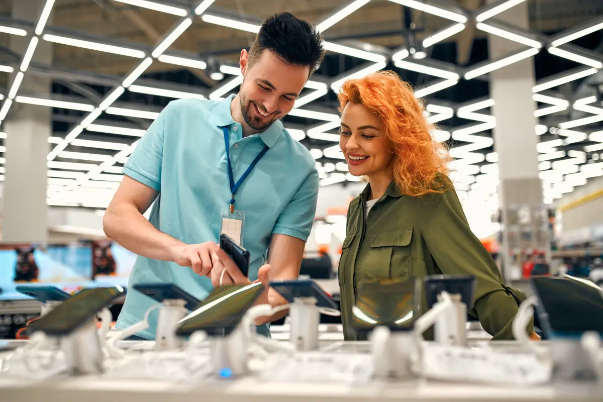 Sales associate assisting a customer with smartphones displayed in an electronics store.