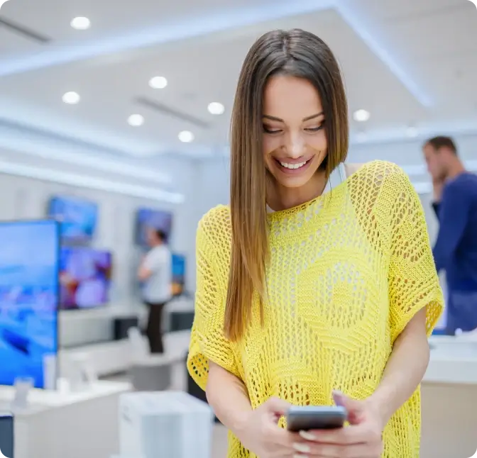 A woman in a yellow top shopping for a smartphone at the Verizon store.