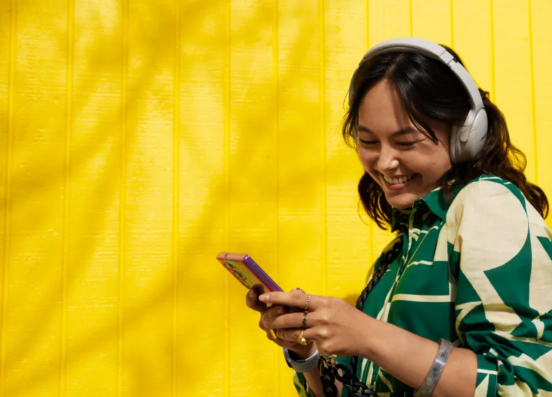 A woman in headphones smiling at her phone